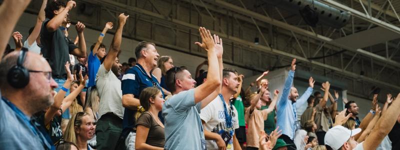 Cheering crowd in a stadium with raised arms, showing excitement and energy.
