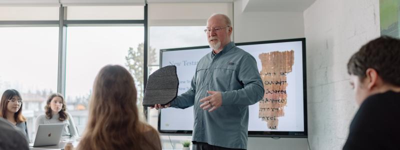 A New Testament professor teaches students in a classroom with a slide displaying an ancient manuscript.