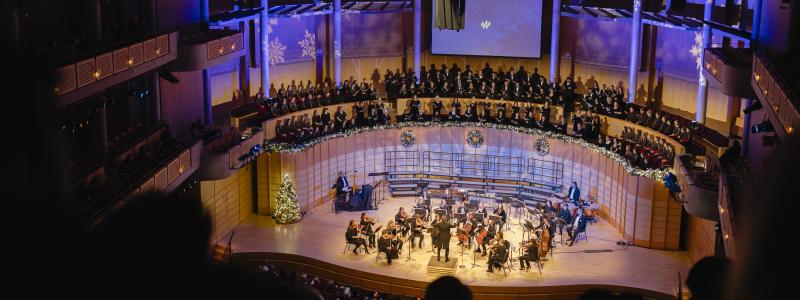 Concert hall with orchestra, choir, and blue-lit snowflake decorations.
