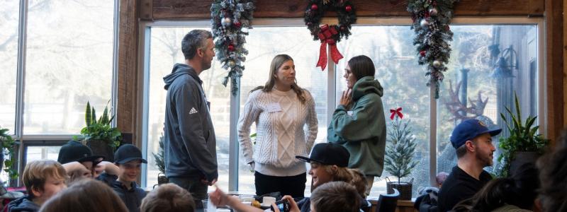 People standing indoors by decorated windows with wreaths.