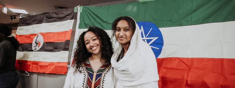 Two people smiling in front of Ethiopian and Ugandan flags.