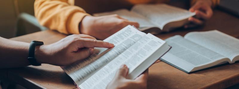 People reading and discussing books at a wooden table.