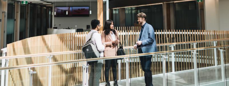 Three people talking in a bright, modern office hallway.