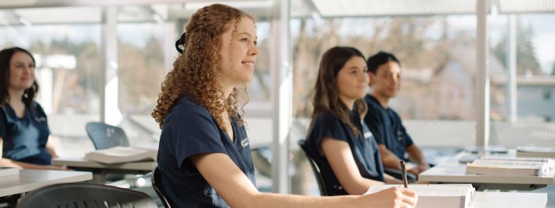 Students attentively listening in a sunlit classroom.