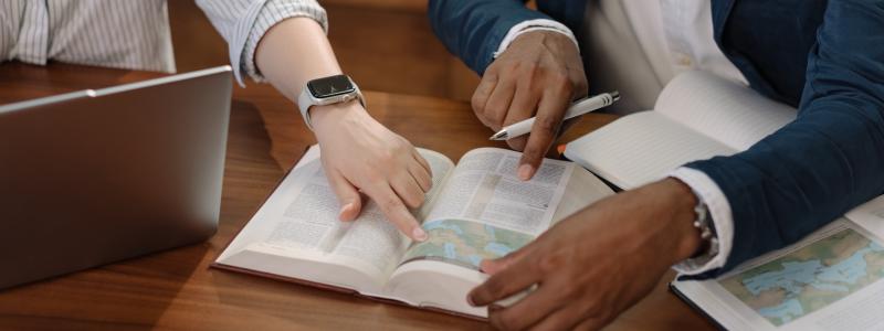 Two people pointing at a Bible, working together at a table.