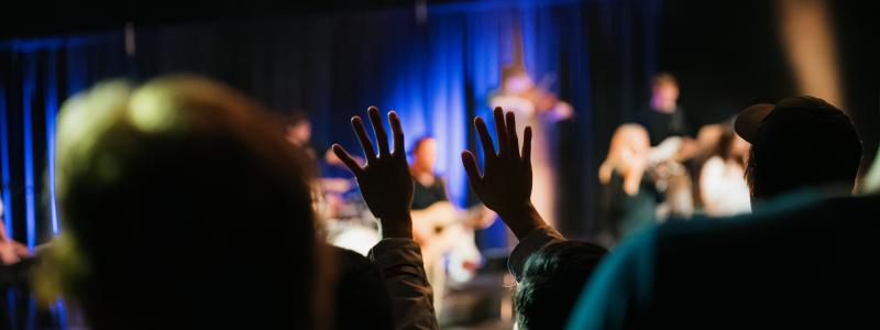 Concert audience with hands raised, spotlight on stage.
