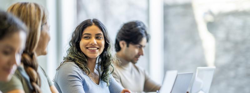 Students using laptops and discussing in a bright study room.