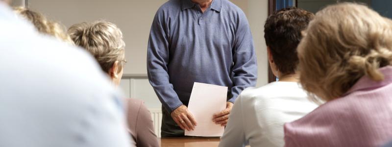 Man standing and smiling in front of a seated group in a classroom.