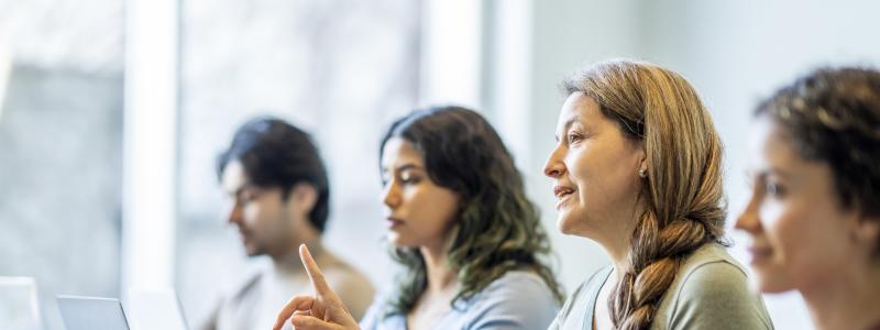 Four people seated at a table with laptops, engaged in discussion.