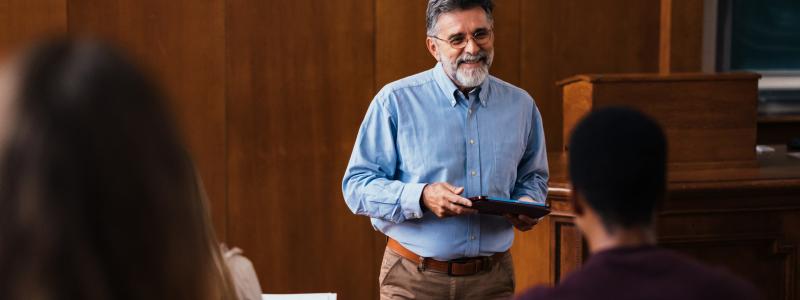 Professor lecturing in a classroom with students listening.