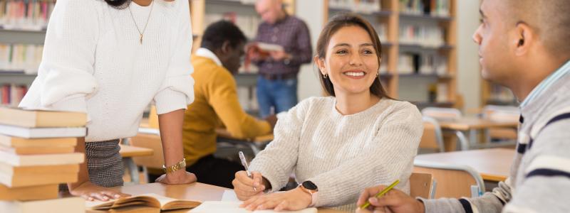 People studying together in a bright library, smiling and discussing.