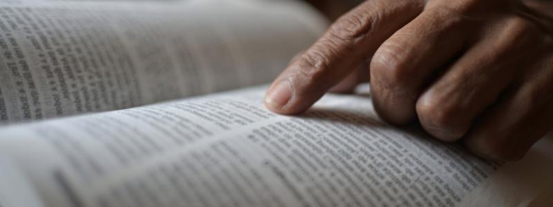 Finger pointing at text in an open book.