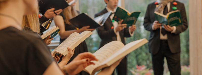 TWU Chamber Choir hold songbooks and sing with plastic coloured lights draped around their shoulders.