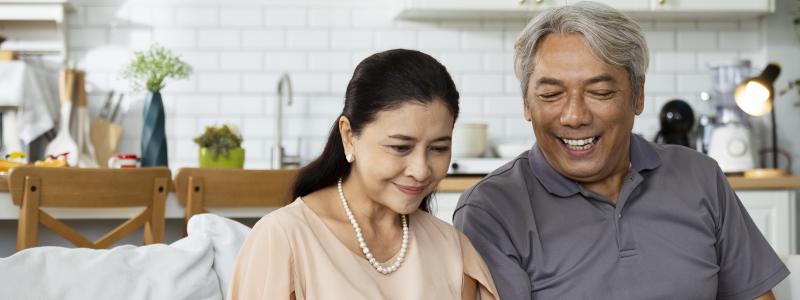 Couple seated on sofa and smiling while looking at laptop