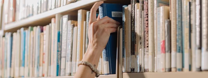 hand grabbing a book of a library bookshelf