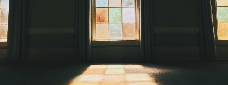 Sunlight streaming through tall arched stained‑glass windows, casting colorful light onto the floor of a dimly lit room.