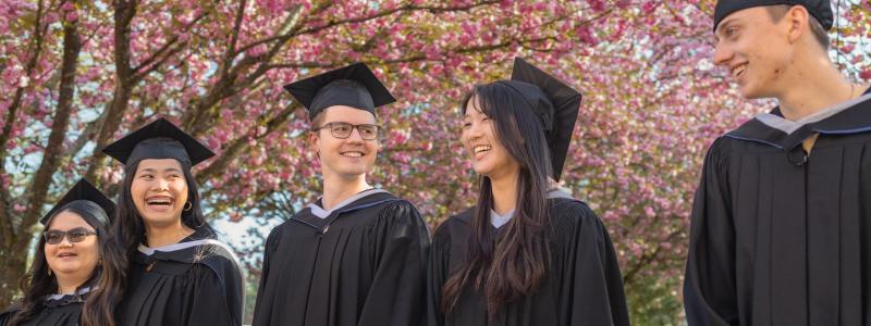 graduates in regalia walking in front of cherry blossoms