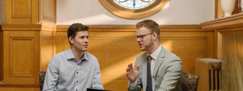 Students sitting at a table talking with a stained glass window behind them