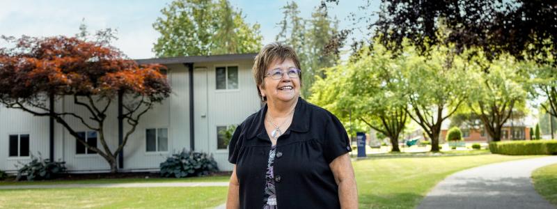 Patti Victor Switametelót on campus in front of Douglas Centre with a blue sky and trees behind her