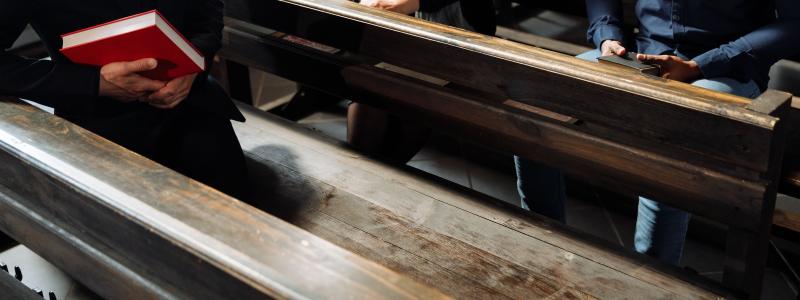 a person holding a book sitting on a bench in the church