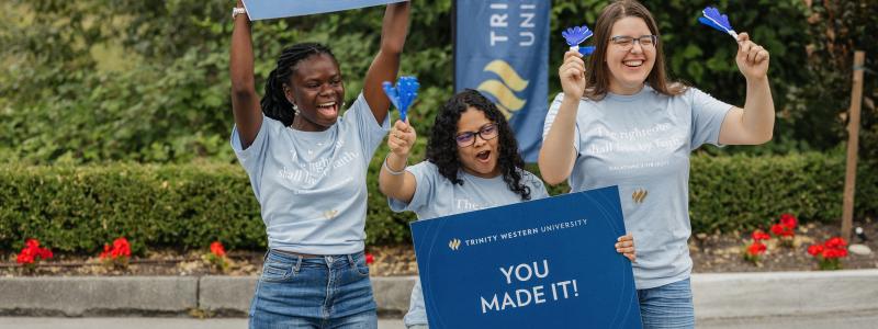 Three TWU students holding welcome signs during orientation day on the Langley campus.