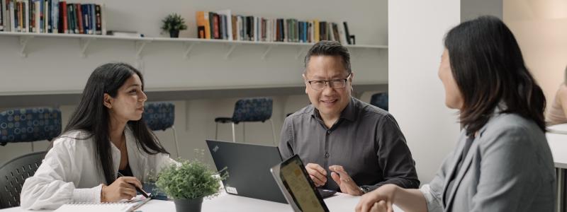 Students and faculty discussing coursework together around a table in a classroom setting.