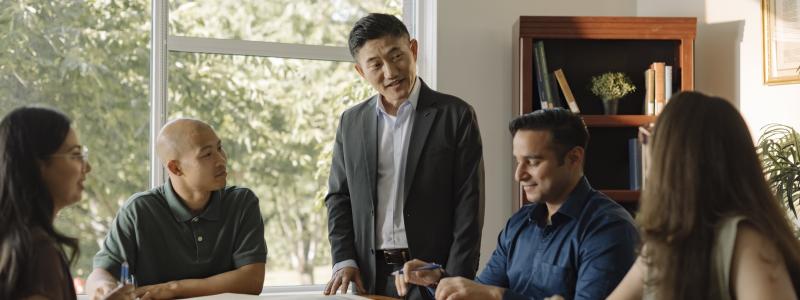 A faculty member leading a discussion with students seated around a table.