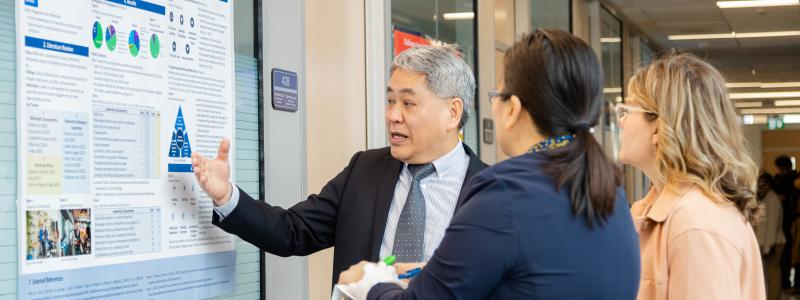 A presenter discusses a research poster with two attendees during a poster presentation.