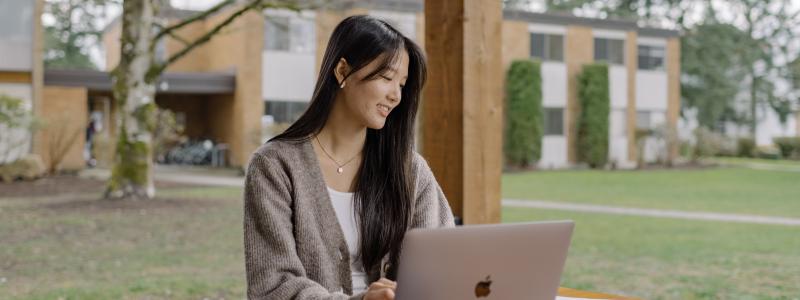 Student working on a laptop at an outdoor table on the TWU campus.