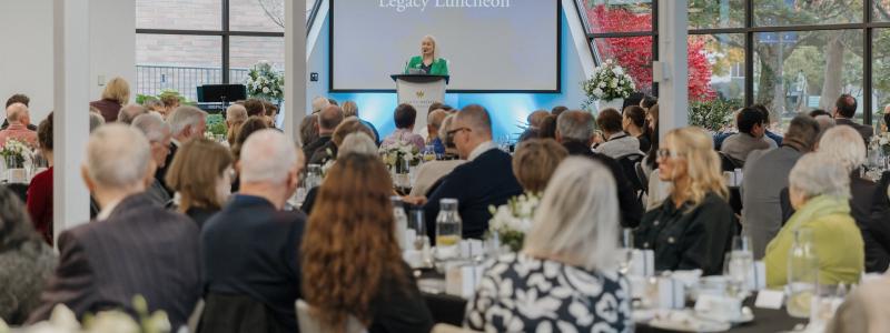 Guests seated at tables in Trinity Commons during Trinity Western University’s Legacy Luncheon, with a speaker presenting at the podium.