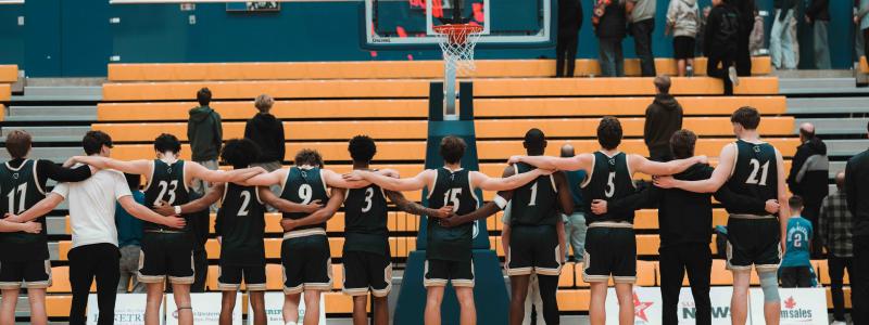 Basketball players stand together on a gymnasium court before a game.