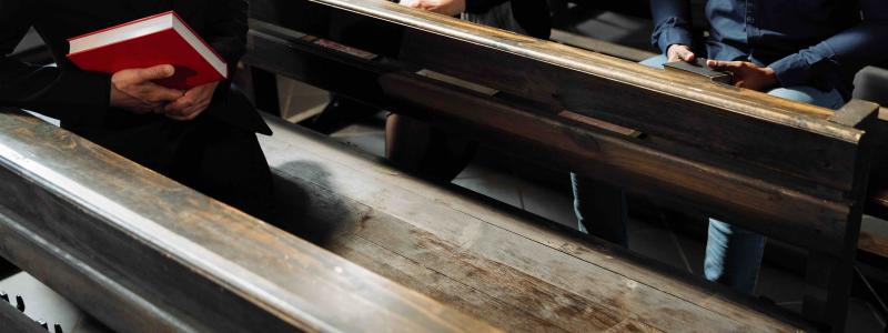 a person holding a book sitting on a bench in the church