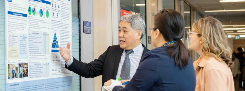 A presenter discusses a research poster with two attendees during a poster presentation.