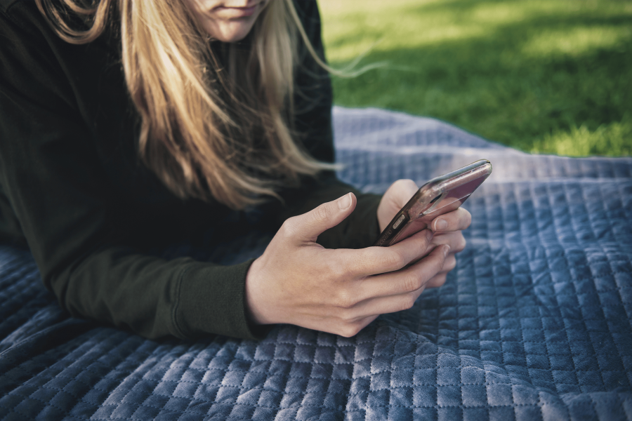 white woman on phone laying on blanket on grass