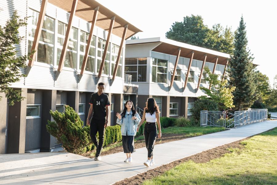 Three students walking on campus outside music building talking.