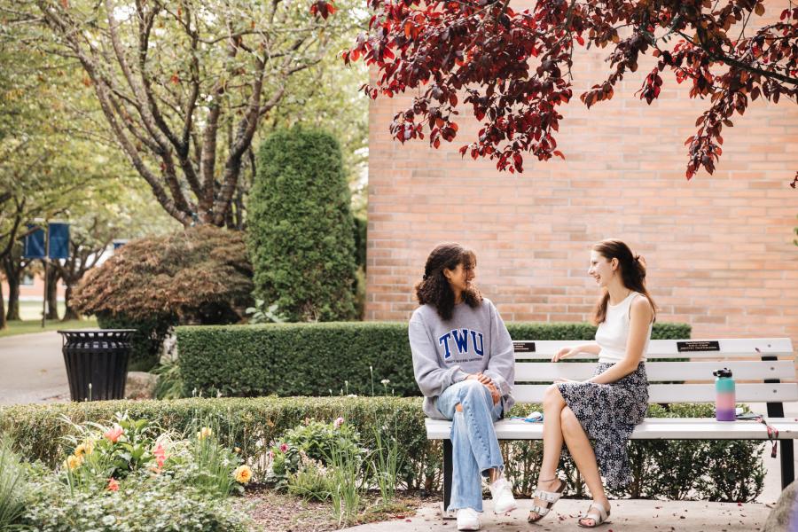 Two female students sitting on a bench talking at the TWU Langley campus.