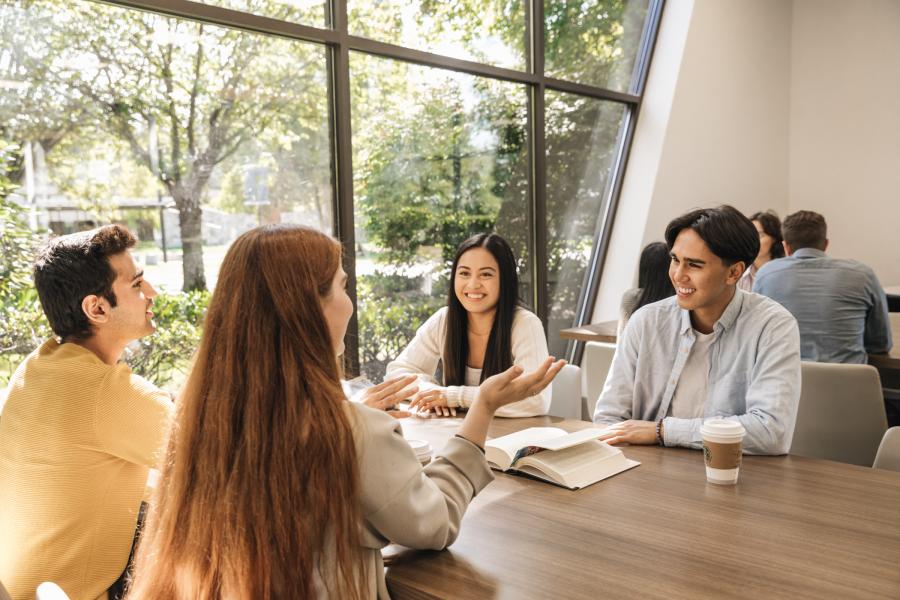 Four students sitting down, reading a book and talking at the Trinity Commons