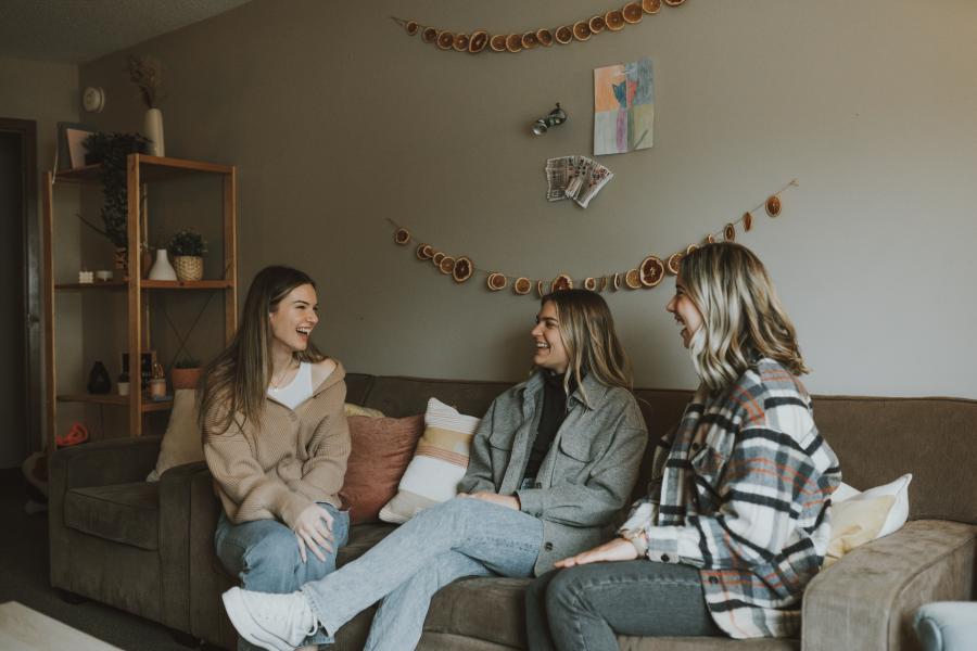 Three female students sitting on a couch in their dorm apartment.