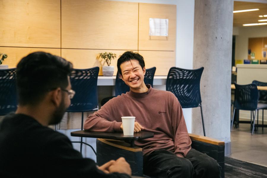 Two males sitting, talking, and smiling over coffee.