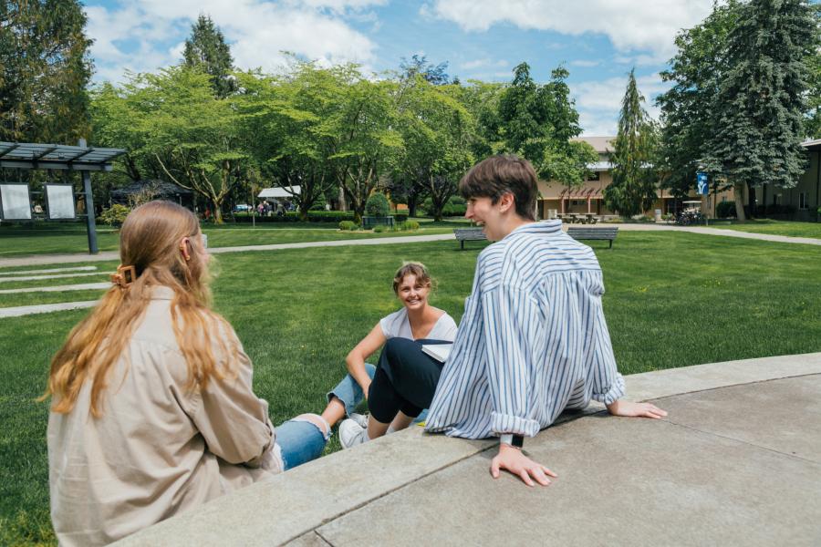 Three female students sitting on the steps of the outdoor chapel, smiling and talking