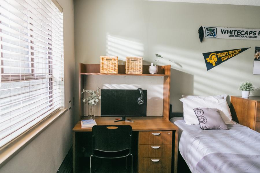 A dorm room with a desk, bed, and wall decorations. 