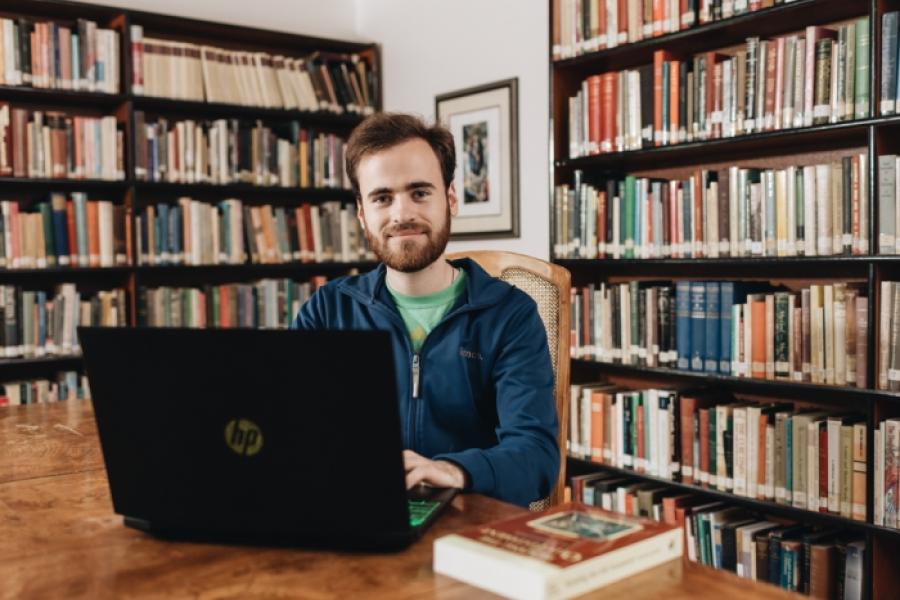 male student sitting in the library of the Catholic Pacific College smiling over his open laptop.