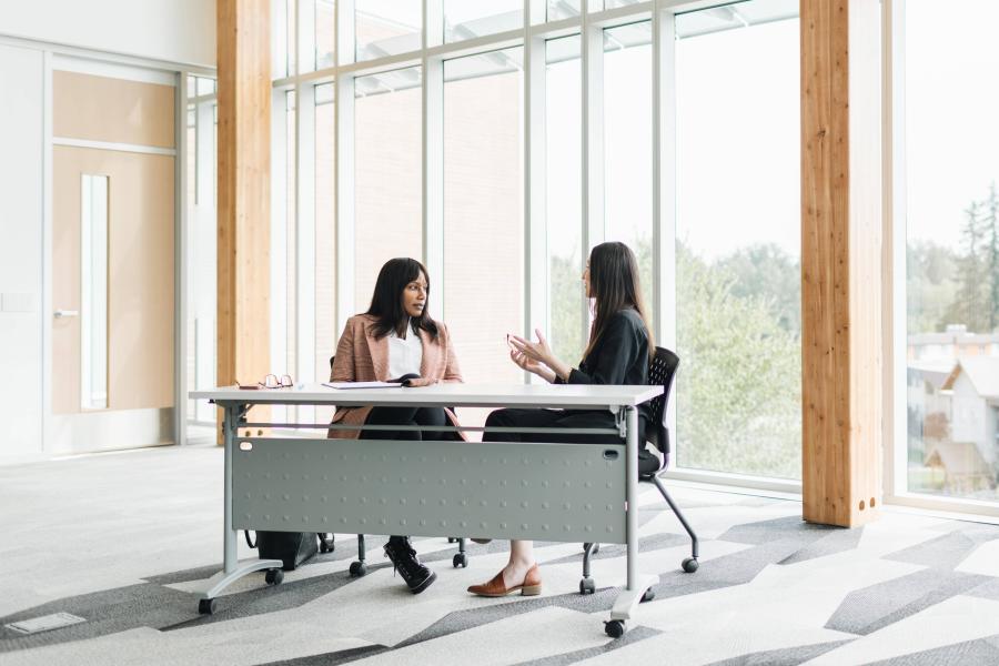 two women sitting at table talking to each other