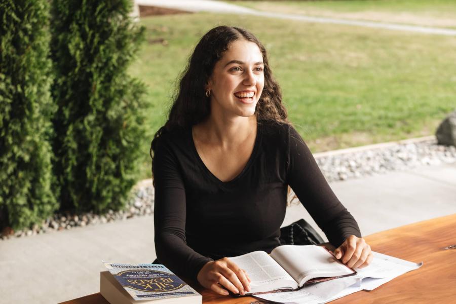 female student sitting outside at table with books