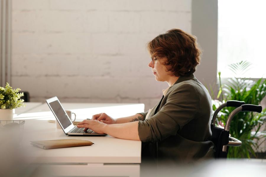 women in a wheelchair sitting at desk and working on a laptop