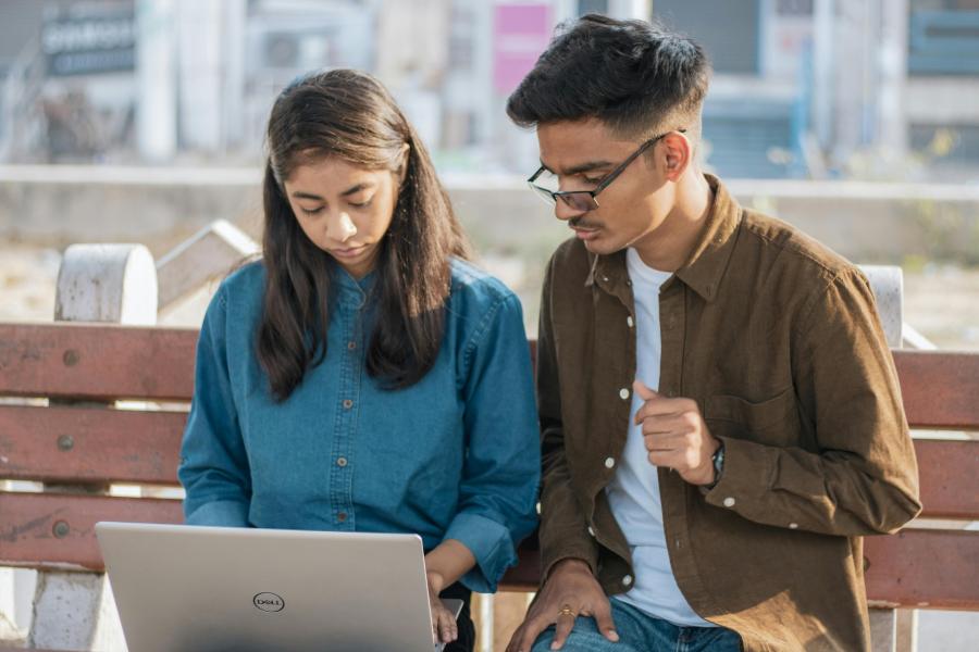 women with laptop and man sitting on bench outside