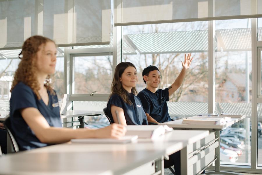 A nursing student in class raising his hand to ask a question.