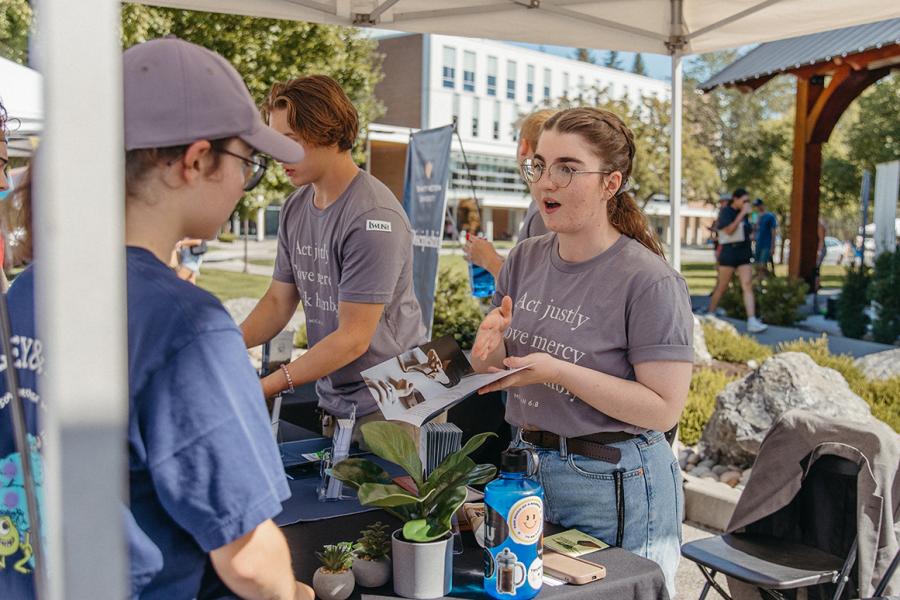 student talking to someone at a booth outside in a tent