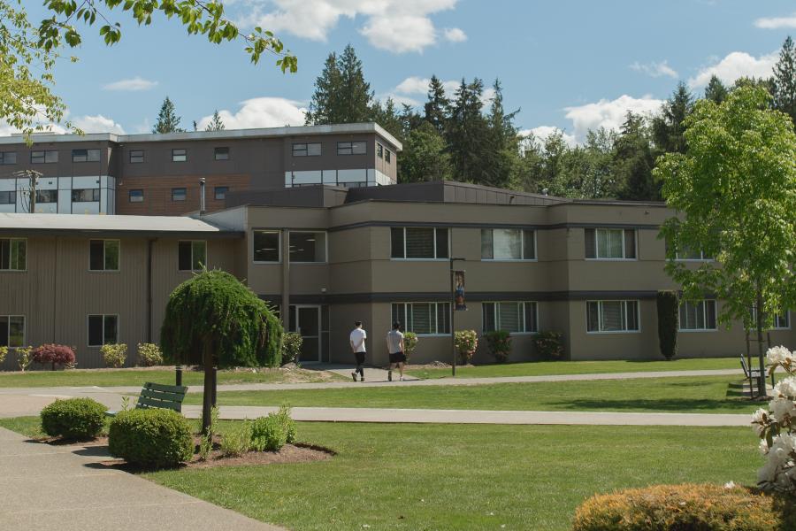 Sunny day at a campus with a modern building, trees, and a walkway.