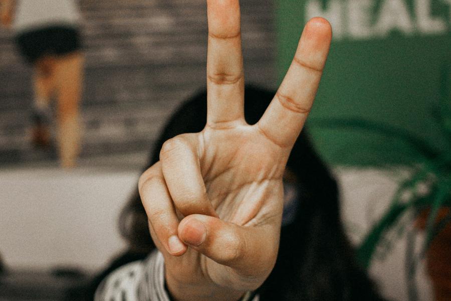Hand showing a peace sign in front of blurred background.
